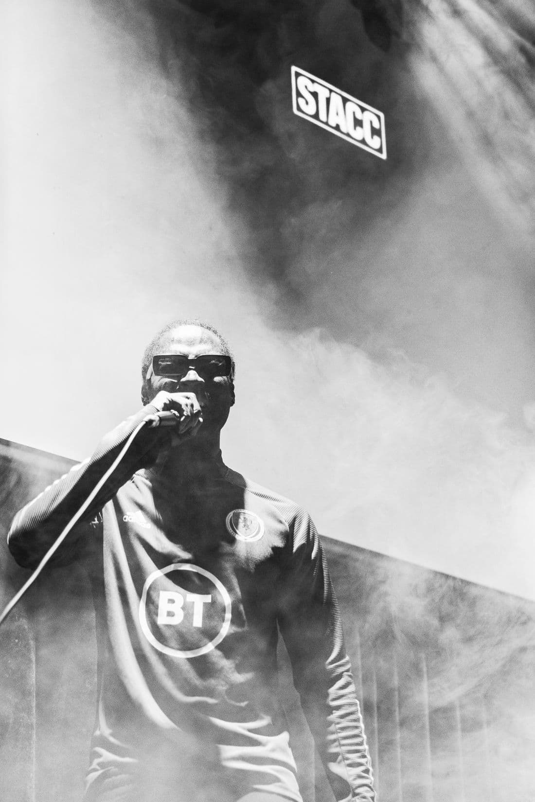 An MC performing through stage smoke under the STACC sign, in black and white